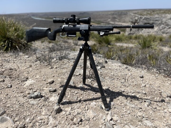 A rifle is on top of a tripod in the desert.